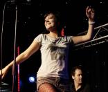 Sur scène, Lily Allen garde sa bonne humeur. Collants résille et mini short, la chanteuse montre ses nouvelles formes.  