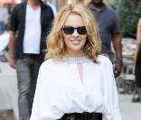 La chanteuse Kylie Minogue très chic et estival dans une petite robe blanche façon tunique, joliment rehaussée d'une large ceinture noire, portée avec de ravissantes sandales argentées et une paire de Ray-Ban sur le nez.