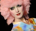 Zoom sur un top du défilé printemps-été 2009 de John Galliano, la jeune femme coiffée d'une perruque rose et maquillée à outrance offre une vue spectaculaire de sa tenue multicolore. 