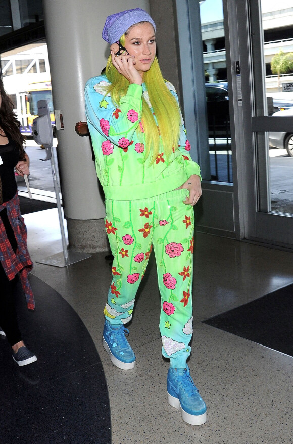 Kesha, les cheveux jaune, arrive à l'aéroport de LAX pour prendre l’avion. La coque de téléphone de Kesha est une poupée en 3D! Le 4 juillet 2015