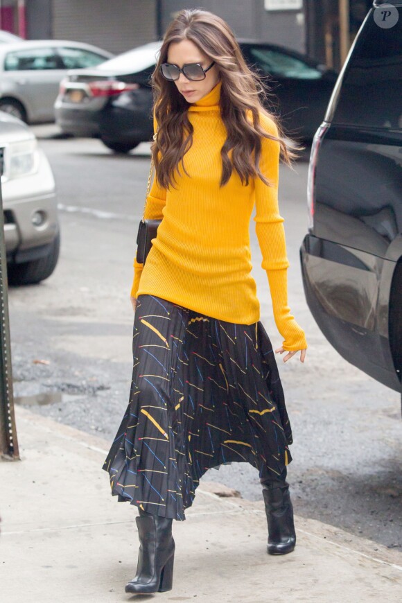Victoria Beckham arrive au studio de sa marque de vêtements (Victoria Beckham) à New York, habillée d'un pull à col roulé, une jupe plissée, un sac noir et des bottines noires Victoria Beckham. Le 8 février 2016.