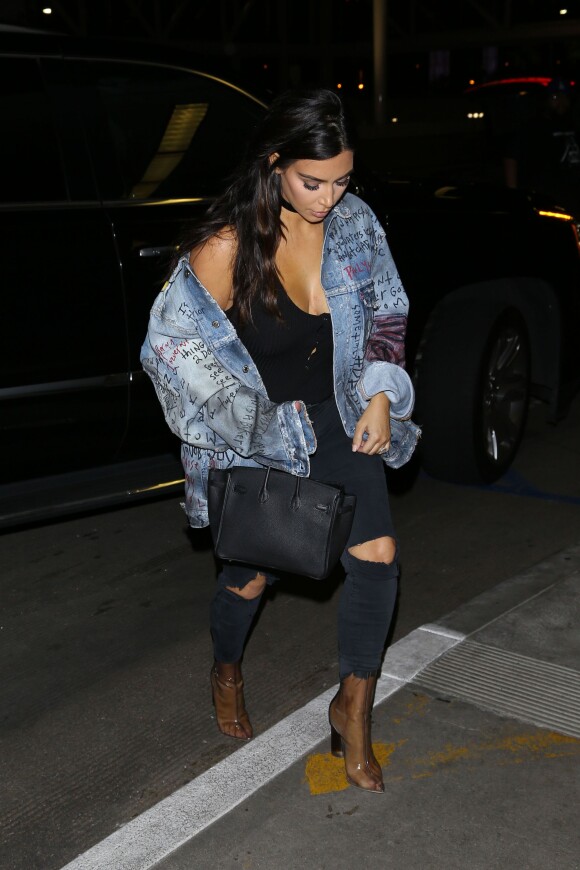 Kim Kardashian surprise à l'aéroport LAX à Los Angeles, porte une veste en denim custom Himumimdead, un body noir The Line by K, un jean J Brand, un sac Hermès (modèle Birkin) et des bottines en plexiglas YEEZY (collection Season 3). Le 11 avril 2016.