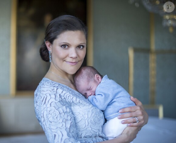 La princesse Victoria de Suède tenant le prince Oscar dans ses bras, photo réalisée par Kate Gabor et publiée par la cour royale de Suède le 24 mars 2016, soit trois semaines après la naissance du bébé.