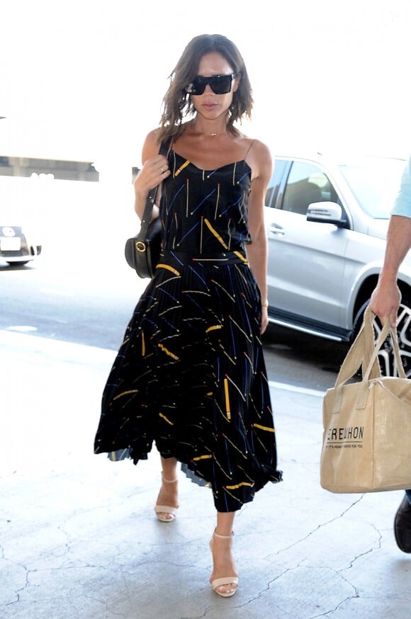Victoria Beckham à l'aéroport LAX à Los Angeles, porte un haut et une jupe plissée Victoria Beckham (pré-collection automne-hiver 2016), un sac Victoria Beckham (modèle Half Moon) et des sandales beiges. Le 1er août 2016.