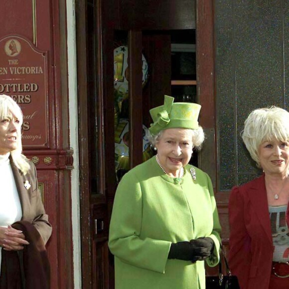 Barbara Windsor (en tailleur rouge) recevant la visite de la reine Elizabeth II et du duc d'Edimbourg sur le tournage du soap opera EastEnders en novembre 2001 à Londres.