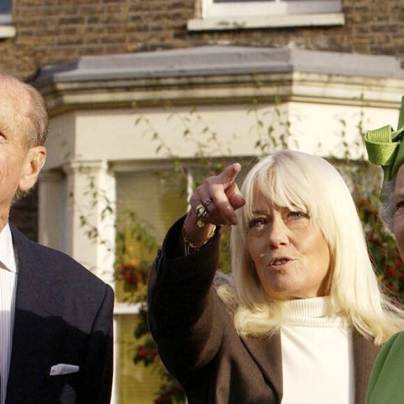 Barbara Windsor (en tailleur rouge) recevant la visite de la reine Elizabeth II et du duc d'Edimbourg sur le tournage du soap opera EastEnders en novembre 2001 à Londres.