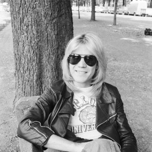 En France, à Paris, portrait de Patrick Juvet en blouson de cuir, portant une paire de lunettes de soleil, assis sur un banc, souriant en extérieur; plan de face . Le 14 mai 1974. © Bruno Schneider via Bestimage