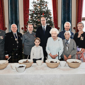 Le prince George de Cambridge prépare, sous le regard bienveillant du prince William, duc de Cambridge, du prince Charles, prince de Galles et de la reine Elisabeth II, des puddings de Noël, dans le cadre du lancement de l'initiative 'Together at Christmas' de la Royal British Legion au Palais de Buckingham, le 21 décembre 2019.