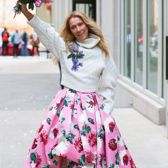 Celine Dion rayonnante et très souriante dans un ensemble pull écru et jupe bouffante fleurie salue ses fans à la sortie de son hôtel à New York, le 8 mars 2020