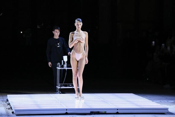 Bella Hadid arrive sur le podium vêtue d'une simple culotte, c'est alors que trois hommes pulvérise une solution sur le mannequin américain et en quelques minutes, une robe minimaliste à manches à épaules dénudées et fente latérale à été créée en clôture du défilé Coperni Collection Femme Prêt-à-porter Printemps/Eté 2023 lors de la Fashion Week de Paris (PWF), France, le 30 septembre 2022. 