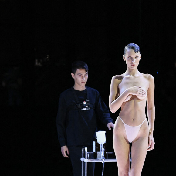 Bella Hadid arrive sur le podium vêtue d'une simple culotte, c'est alors que trois hommes pulvérise une solution sur le mannequin américain et en quelques minutes, une robe minimaliste à manches à épaules dénudées et fente latérale à été créée en clôture du défilé Coperni Collection Femme Prêt-à-porter Printemps/Eté 2023 lors de la Fashion Week de Paris (PWF), France, le 30 septembre 2022. 