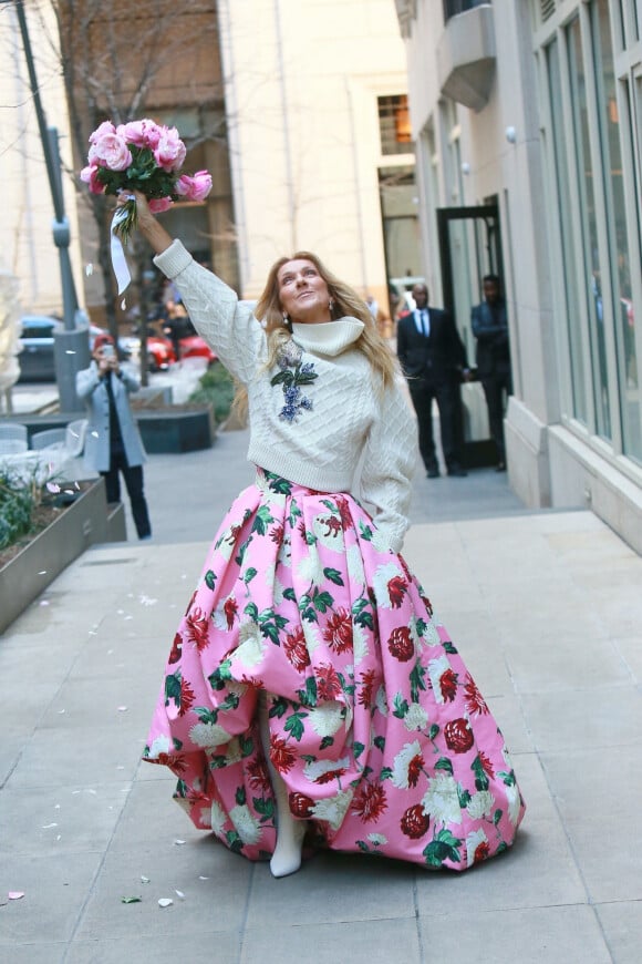 Céline Dion rayonnante et très souriante dans un ensemble pull écru et jupe bouffante fleurie salue ses fans à la sortie de son hôtel à New York, le 8 mars 2020.