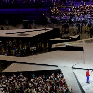 Léon Marchand porte la flamme olympique aux côtés de de Thomas Bach, président du CIO et Teddy Riner pour le passage de relais entre les jeux olympiques et paralympiques à Paris pendant la cérémonie de clôture des Jeux Olympiques de Paris 2024 au stade de France à Saint-Denis, le 11 août 2024