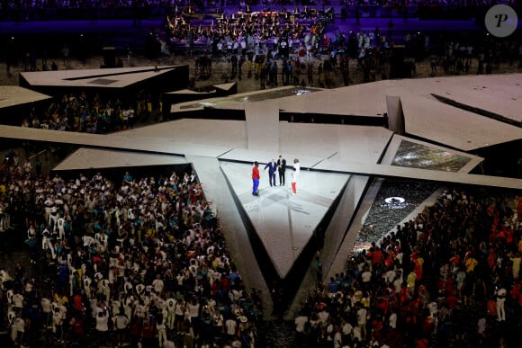 Léon Marchand porte la flamme olympique aux côtés de de Thomas Bach, président du CIO et Teddy Riner pour le passage de relais entre les jeux olympiques et paralympiques à Paris pendant la cérémonie de clôture des Jeux Olympiques de Paris 2024 au stade de France à Saint-Denis, le 11 août 2024