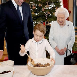 Le prince George de Cambridge prépare, sous le regard bienveillant du prince William, duc de Cambridge, du prince Charles, prince de Galles et de la reine Elisabeth II, des puddings de Noël, dans le cadre du lancement de l'initiative 'Together at Christmas' de la Royal British Legion au Palais de Buckingham, le 21 décembre 2019. 