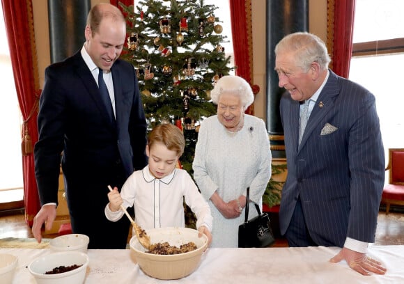 Le prince George de Cambridge prépare, sous le regard bienveillant du prince William, duc de Cambridge, du prince Charles, prince de Galles et de la reine Elisabeth II, des puddings de Noël, dans le cadre du lancement de l'initiative 'Together at Christmas' de la Royal British Legion au Palais de Buckingham, le 21 décembre 2019. 