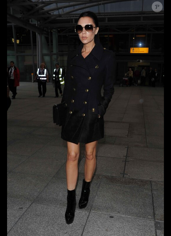 Victoria Beckham mise pour un look sûr en manteau Burberry, lunettes oversize et bottines noires. 