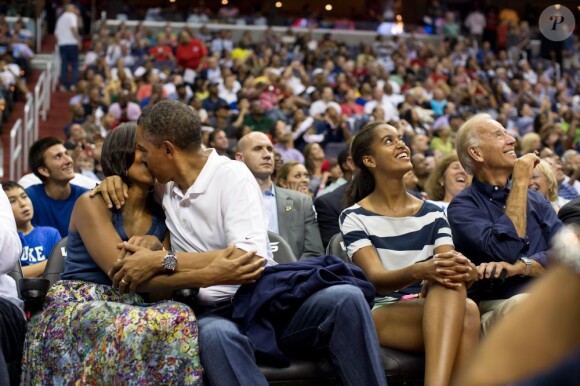 Michelle et Barack Obama, surpris par la Kiss Cam du stade, s'embrassent durant un match de basket-ball opposant l'équipe de Brésil aux États-Unis. À leurs côtés, leur fille aînée Malia et le vice président Joe Biden. À Washington, le 16 juillet 2012.