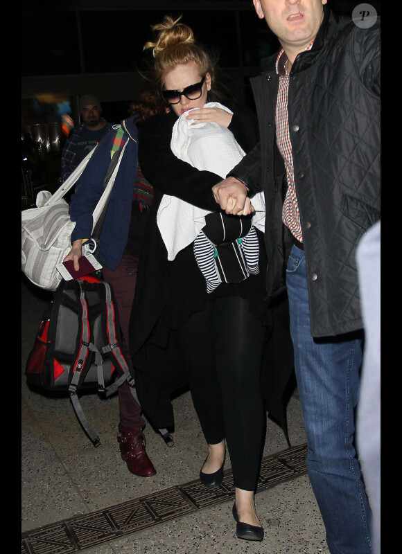 Arrivée tumultueuse pour la chanteuse Adele qui essaie de protéger son nouveau-né des photographes et de la foule, à l'aéroport de Los Angeles, le 10 janvier 2013.