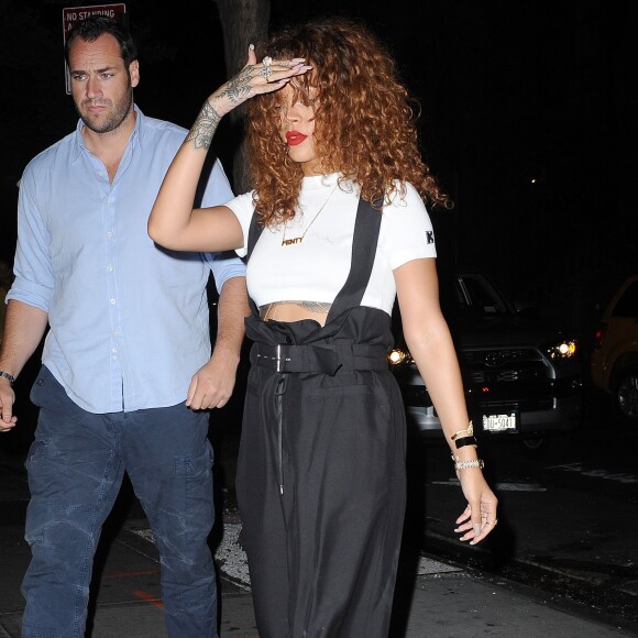 Pour aller au studio, Rihanna opte pour un tee shirt crop-top blanc Kiko Mizuhara porté avec un pantalon taille haute à bretelles Jean Paul Gaultier et des sandales noires compensées Chanel, le 16 juillet 2015 à New York