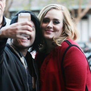 La chanteuse Adele souriante à New York le 20 novembre 2015. Elle porte un long gilet rouge à franges et continue les selfies avec ses fans.