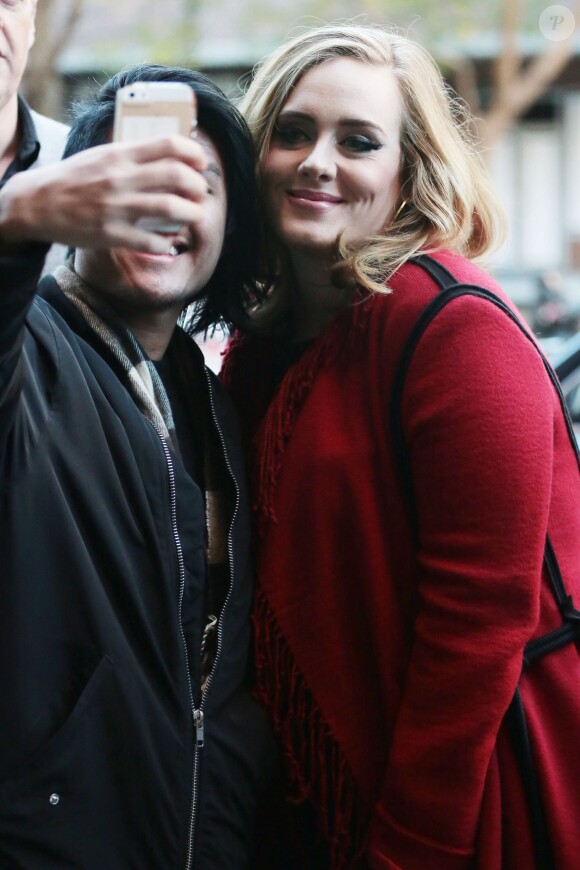La chanteuse Adele souriante à New York le 20 novembre 2015. Elle porte un long gilet rouge à franges et continue les selfies avec ses fans.