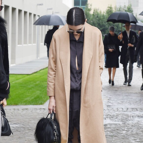 Kendall Jenner photographiée à l'issue du défilé Bottega Veneta à Milan, porte un manteau en laine camel AYR (modèle The Robe), une combinaison en soie One Teaspoon (modèle Love Machine) et des baskets adidas. Des lunettes de soleil Ahlem (modèle Concorde) et un sac noir, accessoirisé d'un pompom Fendi, complètent sa tenue. Le 27 février 2016.