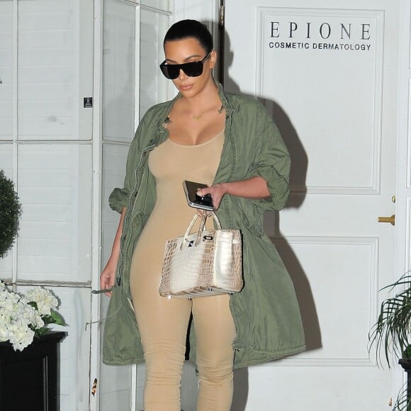 Kim Kardashian à la sortie du centre dermatologique Epione à Beverly Hills, porte une parka kaki, un body beige, et des sandales transparentes Prada (collection printemps-été 2010). Des lunettes de soleil Saint Laurent et un sac Hermès complètent sa tenue. Le 2 mars 2016.