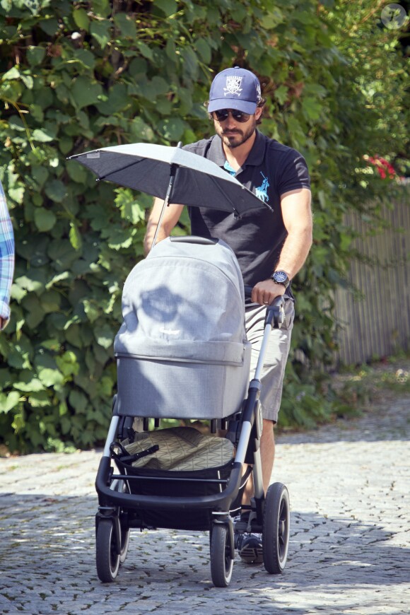 Le prince Carl Philip de Suède promène son fils le prince Alexander pendant que la princesse Sofia assiste à un séminaire à Bastad, la ville où ils se sont connus, le 4 août 2016. Il est accompagné d'un garde du corps qui promène le chien de la famille, Siri.