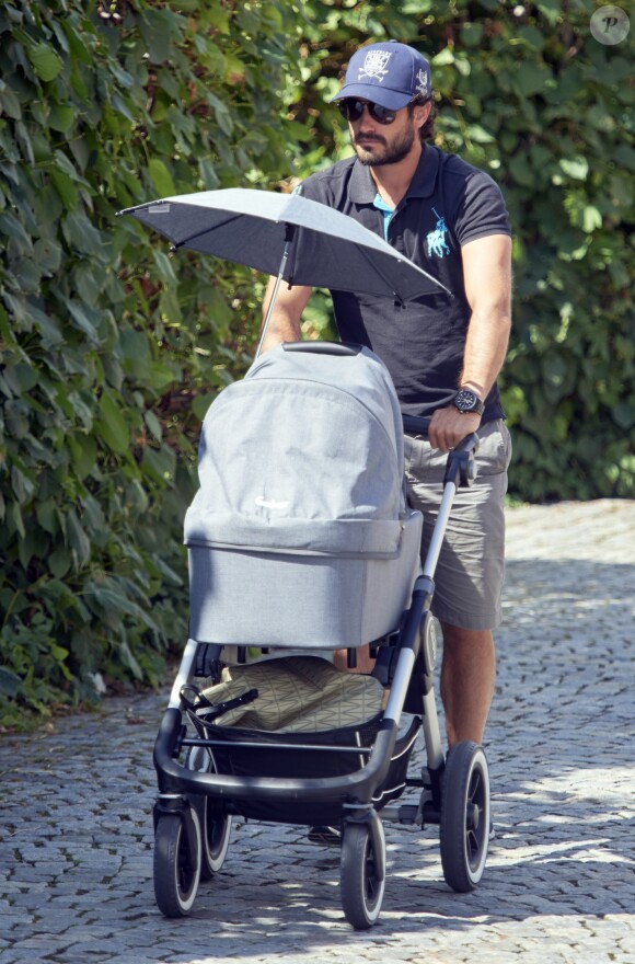 Le prince Carl Philip de Suède promène son fils le prince Alexander pendant que la princesse Sofia assiste à un séminaire à Bastad, la ville où ils se sont connus, le 4 août 2016. Il est accompagné d'un garde du corps qui promène le chien de la famille, Siri.