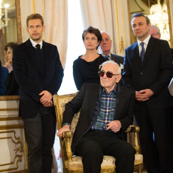 Charles Aznavour est décoré au grade de Commandeur de l'Ordre de la Couronne de Belgique à Bruxelles le 16 novembre 2015. Son fils Nicolas se tient à sa droite derrière lui.