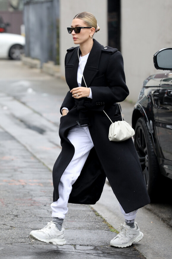 Hailey Baldwin Bieber porte un manteau long noir Saint Laurent, un pull et un jogging Cydnie Jordan et des baskets Balenciaga. Beverly Hills, Los Angeles, le 10 mars 2020
