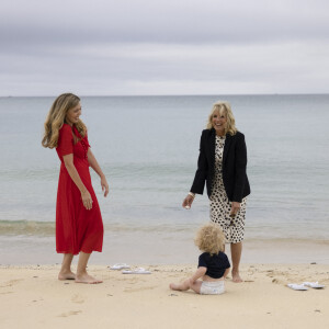 Carrie Johnson s'entretient avec la Première Dame des États-Unis, Jill Biden, lors du sommet des dirigeants du G7 à Carbis Bay, Royaume Uni, le 10 juin 2021, alors que Wilfred Johnson est assis sur la plage.