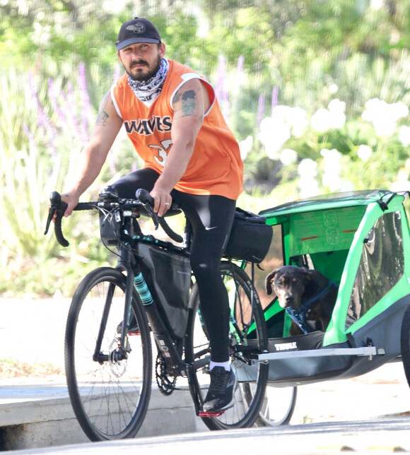 Exclusif - Shia LaBeouf tracte son chien à vélo et sa compagne Mia Goth les suit à Los Angeles le 11 mai 2020.