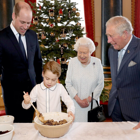 Le prince George de Cambridge prépare, sous le regard bienveillant du prince William, duc de Cambridge, du prince Charles, prince de Galles et de la reine Elisabeth II, des puddings de Noël, dans le cadre du lancement de l'initiative 'Together at Christmas' de la Royal British Legion au Palais de Buckingham, le 21 décembre 2019.