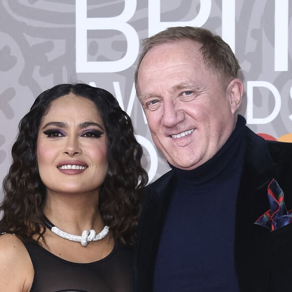 Son habit de nuit s'ouvre légèrement, faisant entrevoir sa poitrine. 
Salma Hayek et son mari Francois-Henri Pinault au photocall de la cérémonie des Brit Awards 2023 à l'O2 Arena à Londres le 11 février 2023.