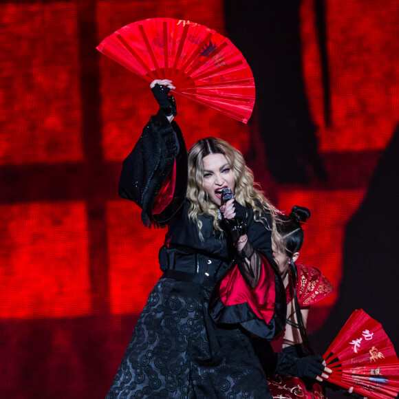 En exécutant un voguing, pratique visant à imiter à la chaîne les gestes des mannequins de magazines, donnant une danse particulière 
Concert de Madonna à l'AccorHotels Arena (Bercy) à Paris, le 9 décembre 2015. 