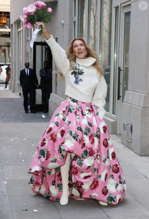 Celine Dion rayonnante et très souriante dans un ensemble pull écru et jupe bouffante fleurie salue ses fans à la sortie de son hôtel à New York, le 8 mars 2020