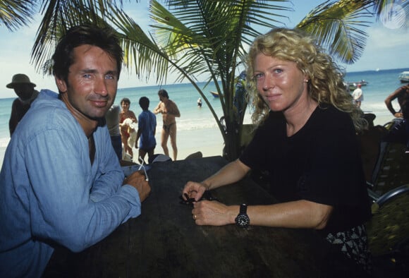 Astrée, quant à elle, exerce ses talents en tant que peintre?
Thierry Lhermitte, très bronzé, assis face à sa femme Hélène, devant un fond de palmes et de mer des Caraïbes. © Alain Canu via Bestimage