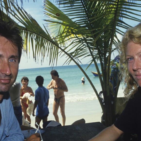 Astrée, quant à elle, exerce ses talents en tant que peintre?
Thierry Lhermitte, très bronzé, assis face à sa femme Hélène, devant un fond de palmes et de mer des Caraïbes. © Alain Canu via Bestimage