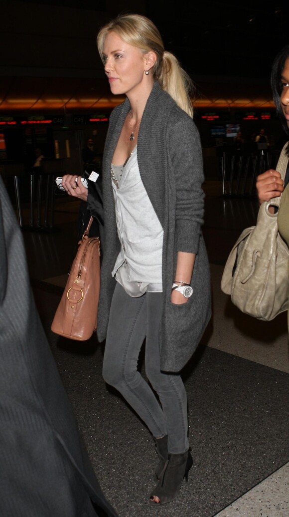 Charlize Theron est une voyageuse stylée, habillée d'un cardigan et d'un slim gris sur des chaussures à bouts ouverts. L'actrice tient un sac Yves Saint Laurent. Aéroport de Los Angeles, le 8 avril 2012.