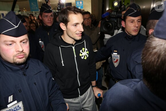 Renaud Lavillenie encadré par la police lors de son arrivée à l'aéroport Paris-Charles de Gaulle après son record du monde du saut à la perche (6,16 m) établi la veille à Donetsk, le 16 février 2014 à Paris