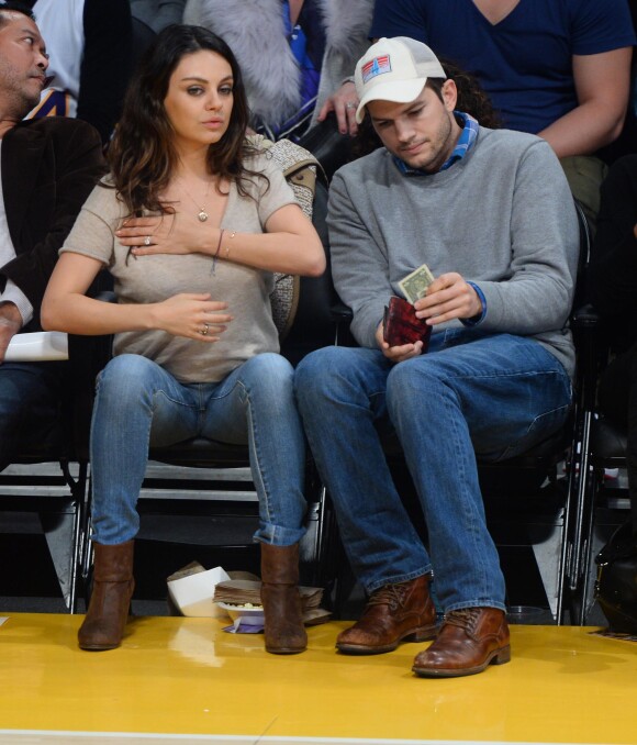 Mila Kunis remet en place son décolleté face à son fiancé Ashton Kutcher pendant le match de basket des Lakers face au Thunder d'Oklahoma City, à Los Angeles, le 19 décembre 2014.
