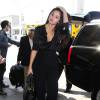 Selena Gomez, toute de noir vêtue avec un chemisier en satin et un pantalon évasé, accessoirise sa tenue d'un sac Prada. Los Angeles, le 18 août 2015.