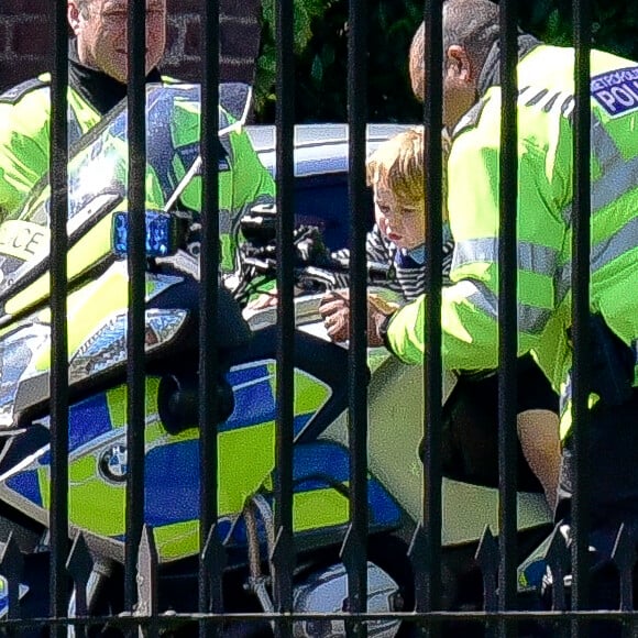 Le prince George de Cambridge est monté sur une moto de la police métropolitaine de Londres le 24 mai 2016 à Kensington Palace, sous les yeux de sa maman Kate Middleton, avec la princesse Charlotte en poussette, après avoir regardé la princesse Anne décoller en hélicoptère pour partir en mission.