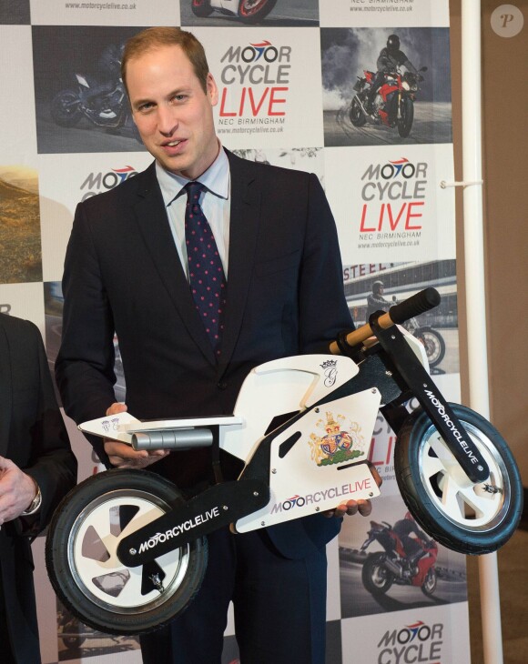 Le prince William, duc de Cambridge, visite le salon de moto Motorcycle Live à Birmingham le 30 novembre 2013 et erçoit en cadeau une petite moto factice pour son fils le prince George.