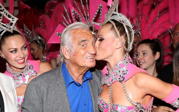 Exclusif - Jean-Paul Belmondo se fait embrasser sur la joue par une danseuse alors qu'il pose dans les coulisses du Moulin-Rouge à Paris le 3 octobre 2016.