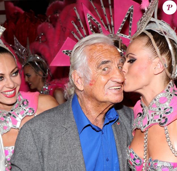 Exclusif - Jean-Paul Belmondo se fait embrasser sur la joue par une danseuse alors qu'il pose dans les coulisses du Moulin-Rouge à Paris le 3 octobre 2016.