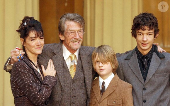 John Hurt en famille lors de la remise de ses insignes de commandeur dans l'ordre de l'empire britannique le 9 décembre 2004, avec sa compagne Anwen et ses fils Alexander (14 ans) et Nicholas (11 ans), issus de son troisième mariage.