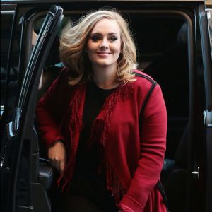 La chanteuse Adele souriante à New York le 20 novembre 2015. Elle porte un long gilet rouge à franges et continue les selfies avec ses fans.